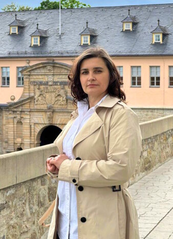 Eine Frau im Mantel steht vor der Zitadelle Petersberg.