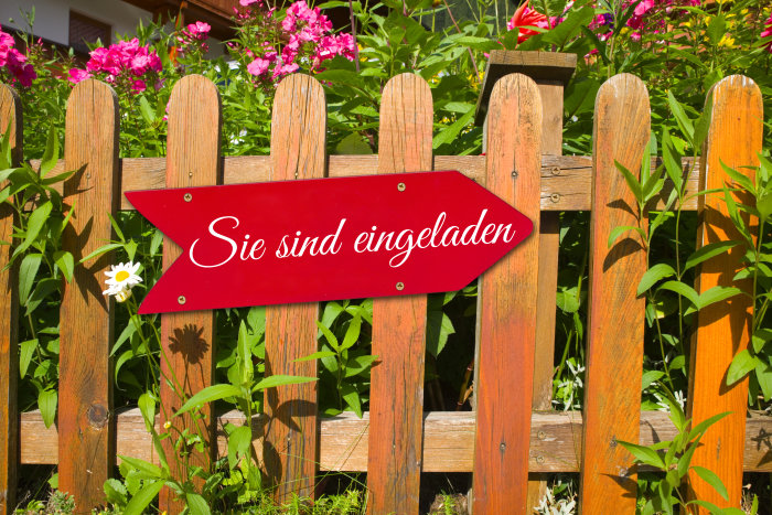 Schild "Sie sind eingeladen" Ein Holzschild mit dem Schriftzug "Sie sind eingeladen" hängt an einem Gartenzaun.