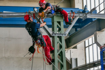 Zwei Höhenretter befinden sich auf einem Strommast und hängen eine Seilrolle ein.