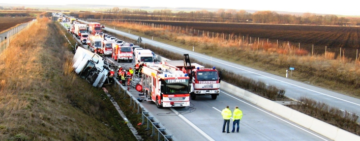Feuerwehr und Rettungsdienstfahrzeuge neben einem umgekippten LKW auf der Autobahn