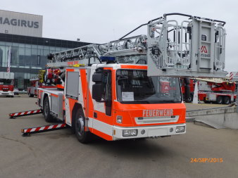 Drehleiter mit Korb der Firma Magirus auf einem Fahrgestell der Firma Iveco mit ausgefahrener Abstützung schräg von vorn fotografiert.