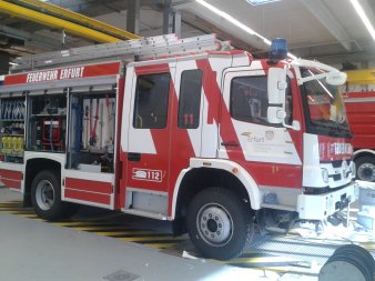 Hilfeleistungs-Löschgruppenfahrzeug HLF 10 der Firma Magirus auf Mercedes-Benz Fahrgestell mit Allradantrieb in der Montagehalle mit offenen Gerätefächern stehend von der Seite fotografiert.