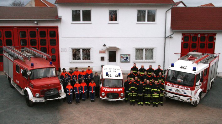 Feuerwehrangehörige der Jugend- und Einsatzabteilung stehen zwischen drei Feuerwehrfahrzeugen vor dem Feuerwehrhaus