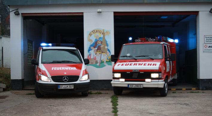 Zwei Feuerwehrfahrzeuge (Transportergröße) halb aus den Fahrzeughallen des Feuerwehrhauses herausgefahren