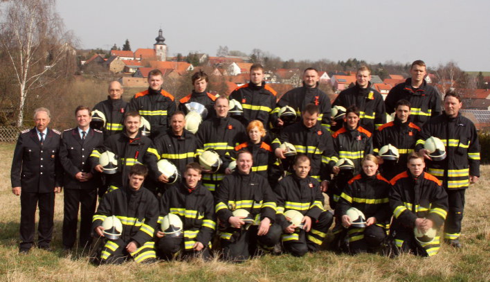 Feuerwehrangehörige in Einsatzbekelidung auf einer Wiese vor der Ortschaft