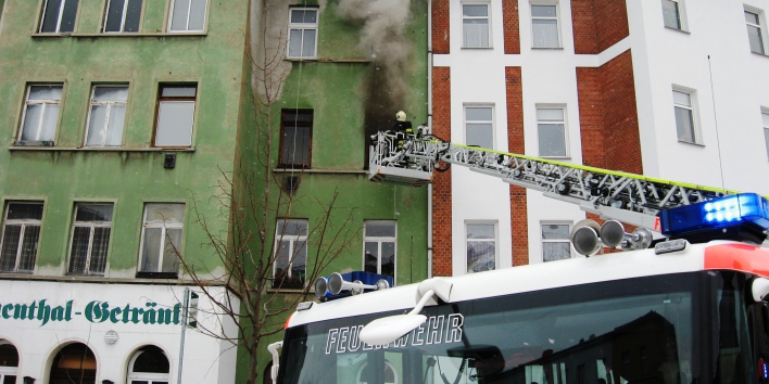 Feuerwehrmann auf Drehleiter bei der Brandbekämfung vor einem Fenster aus dem Rauch kommt