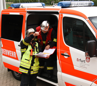 Einsatzleiter und Zugführer im Gespräch vor offener Tür des Kommandowagens mit Feuerwehrplan in den Händen haltend