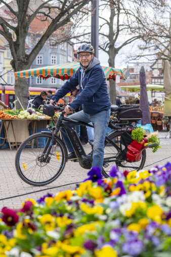 ein Mann sitzt auf einem Fahrrad, im Hintergrund ein Wochenmart
