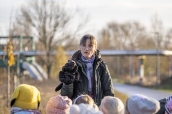 Eine Frau hält eine Handpuppe eines Bibers, im Vordergrund unscharf die Köpfe der Kinder