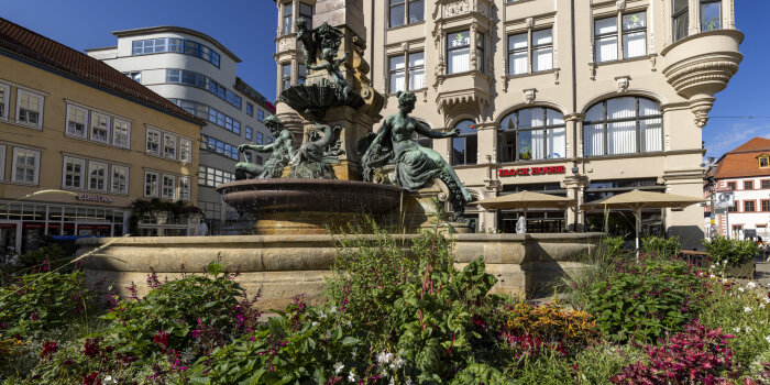 ein Brunnen mit Steinfiguren, umrandet von einem Blumenbeet