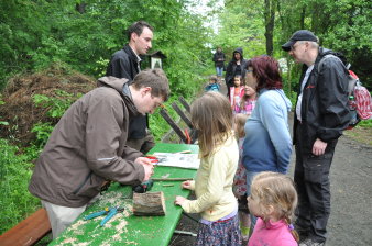 Kinder und Eltern schauen am Infostand interessiert zu, wie Baumteile und Äste fachgerecht beschnitten werden.