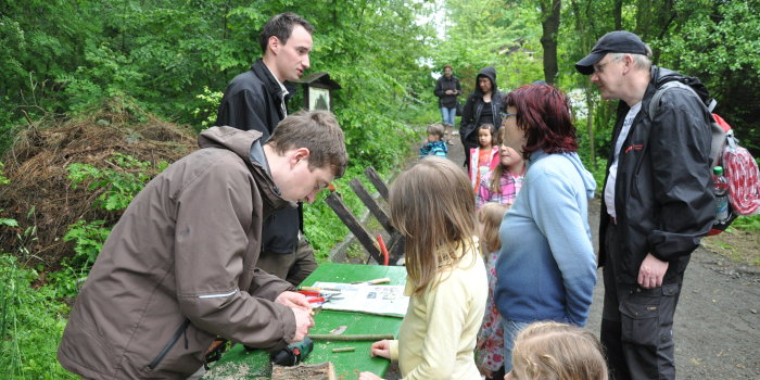 Kinder und Eltern schauen am Infostand interessiert zu, wie Baumteile und Äste fachgerecht beschnitten werden.