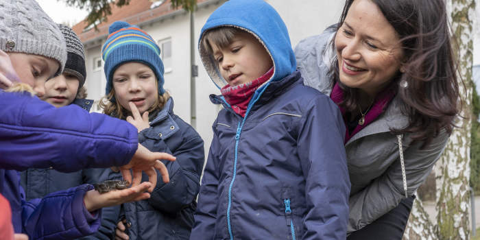 vier Kinder und eine Dame, rechts, in einem Wohngebiet, ein Kind mit Kröte auf der Hand