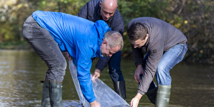 Drei Männer entlehren eine Plastiktüte ins fließende Wasser.