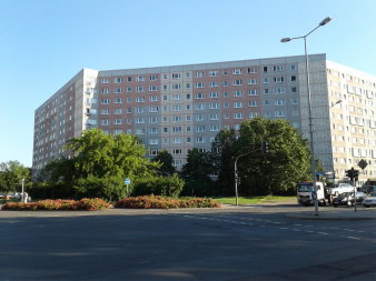 Laubbäume stehen auf Grünfläche vor elfgeschossigem Plattenbau.