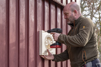 Mann schraubt Schild an Holzwand.