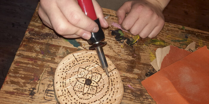 eine Person bearbeitet eine Holzscheibe mit einem Lötkolben