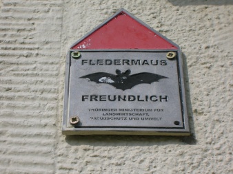 Plakette Fledermausfreundlich. Sie trägt in großen Buchstaben den Schriftzug Fledermaus gefolgt vom Abbild einer Fledermaus und dem Schriftzug freundlich ebenfalls in Großbuchstaben.