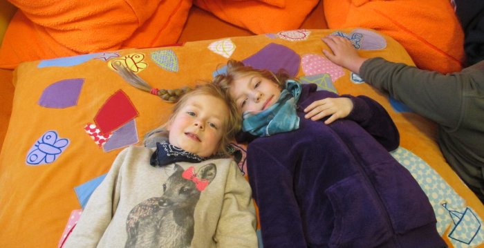 Foto: Titelbild Kinder- und Jugendschutz © Stadtverwaltung Erfurt Zwei Mädchen liegen auf dem Rücken auf einer bunt bestickten gelben Decke