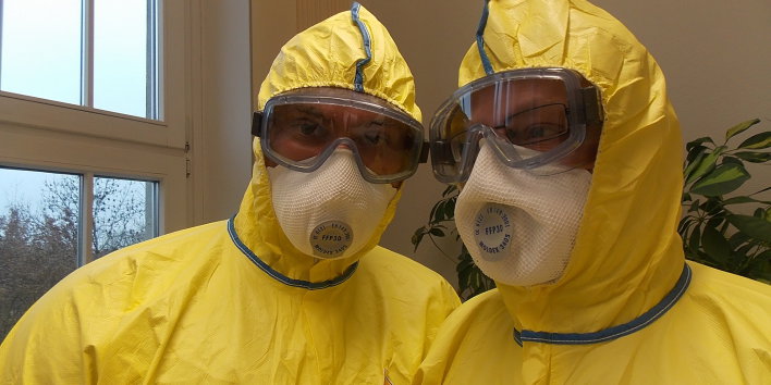 Zwei Personen in gelber Schutzkleidung mit Augen- und Mundschutz
