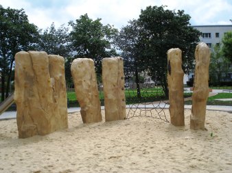 große Sandfläche mit fünf Felsen zum Klettern und schwarzem Kletternetz