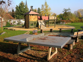 Tischtennisplatte aus Beton und große Sandfläche mit großem rot-gelb-grünen Kletterschloss aus Holz