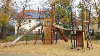 große Sandfläche mit buntem Kletter- und Rutschenturm aus Holz