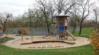 große Sandfläche mit blau-weißem Rutschenturm aus Holz und Kleinkinderschaukel