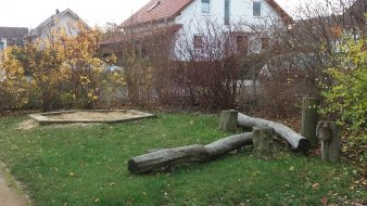 Rasenfläche mit kleinem Sandkasten und Balancierbalken aus Holz