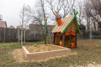 ein Holzhäuschen mit einem Sandkasten auf einem Spielplatz