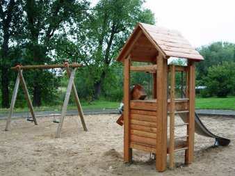 große Sandfläche mit Rutschenturm aus Holz und Schaukel mit zwei Sitzen