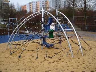 große Sandfläche mit halbrundem Klettergerüst aus Metall und vielen Seilen