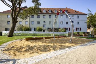 großer Sandspielbereich, im Hintergrund ein Wohnhaus