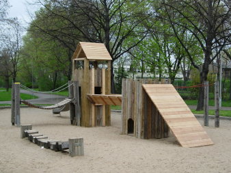 große Sandfläche mit Kletterturm und Balancierbalken aus Holz