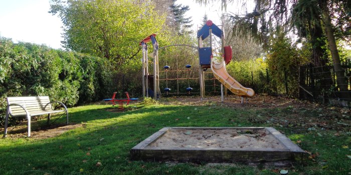 Sandkasten, kleine rot-blaue Federwippe mit zwei Sitzen und gelb-rot-blauer Kletterturm mit Rutsche