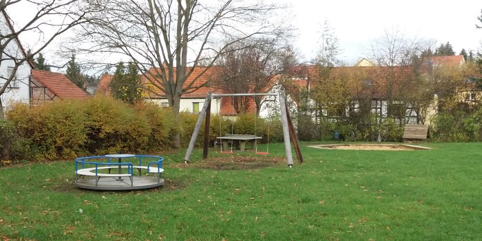 Foto: Spielplatz Am Wolfsbrunnen: Karussell und Doppelschaukel © Stadtverwaltung Erfurt Rasenfläche mit blauem Karussell und Schaukel mit zwei Sitzen
