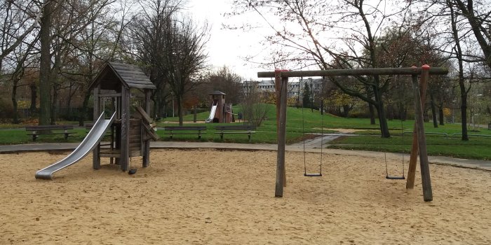 große Sandfläche mit Rutschenturm aus Holz und Schaukel mit zwei Sitzen