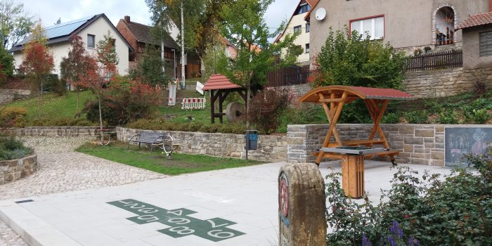 Foto: Spielplatz Wassergraben: Hüpfparcours, Murmelspiel und Sitzhütte © Stadtverwaltung Erfurt grüne Hüpfkästchen mit großen weißen Zahlen von 1 bis 9, viereckiges Labyrinth mit Murmeln und Sitzhütte aus Holz