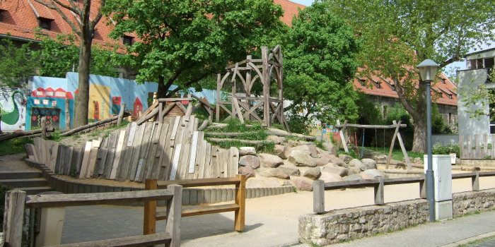 großer Hügel aus Steinen, Holz und Rasen mit Rutschenturm aus Holz und Schaukel mit zwei Sitzen