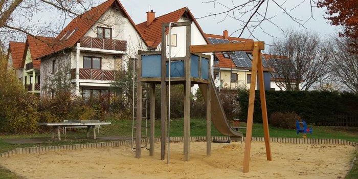 große Sandfläche mit Kletterturm, Rutsche und Schaukel