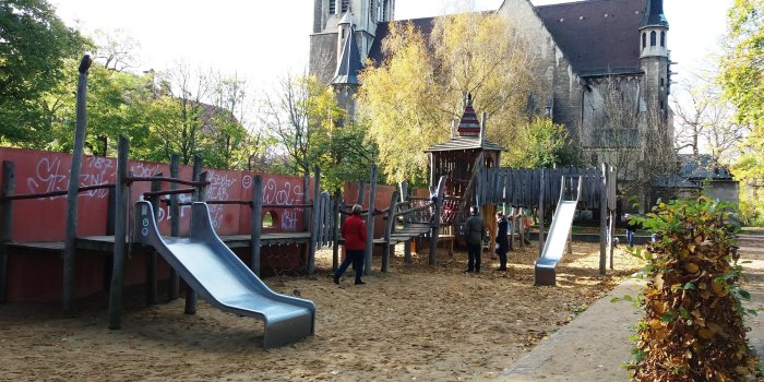 große Sandfläche mit großem Kletterturm aus Holz und zwei Rutschen