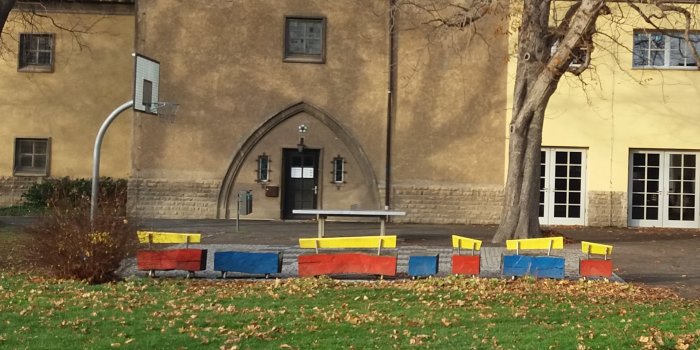 Basketballfläche mit Ständer und Korb und Tischtennisplatte aus Beton und rot-blau-gelber Sitzecke