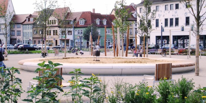 großer Sandkasten umgeben von jungen Bäumen und Sitzmöglichkeiten