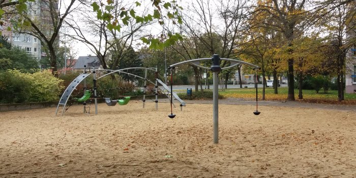 große Sandfläche mit Klettergerüst aus Metall und Karussel mit zwei Sitzen