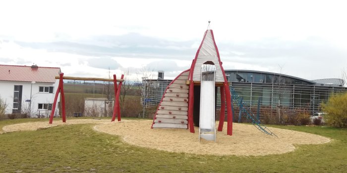 große Sandfläche mit Kletterturm aus Holz mit Rutsche und Schaukel mit zwei Sitzen