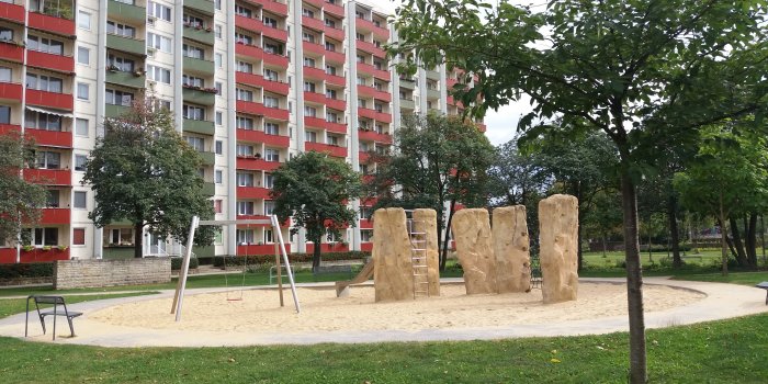 große Sandfläche mit drei Felsen zum Klettern, Rutsche und Schaukel 