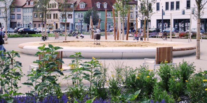 großer Sandkasten umgeben von jungen Bäumen und Sitzmöglichkeiten