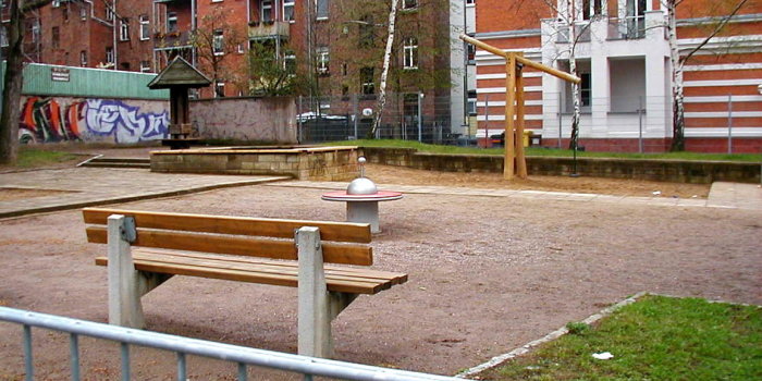 kleine Sandfläche mit Waage aus Holz mit zwei Sitzen und kleines rotes Karussell