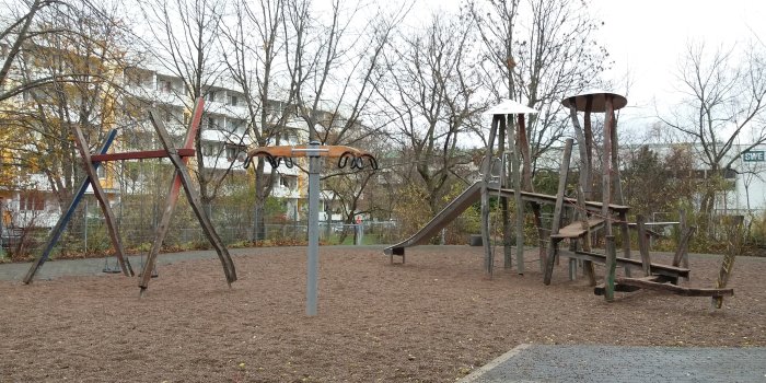 Kiesfläche mit Rutschenturm aus Holz, Drehkarussell und Schaukel mit zwei Sitzen