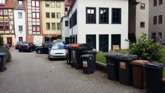 Gepflasterte Fläche, Mülltonnen und Parkplätze vor Häuserreihe